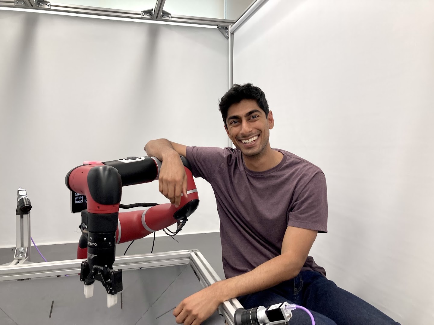 A photo of Akhil Raju. He is sitting down and leaning on a robotic arm.