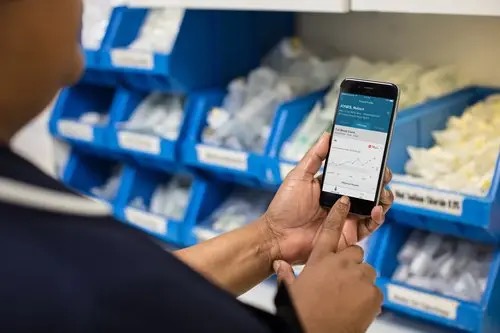 A medical professional uses the Streams app. They are turned away from the camera, we cannot see their face. They are standing in front of boxes of medical equipment.