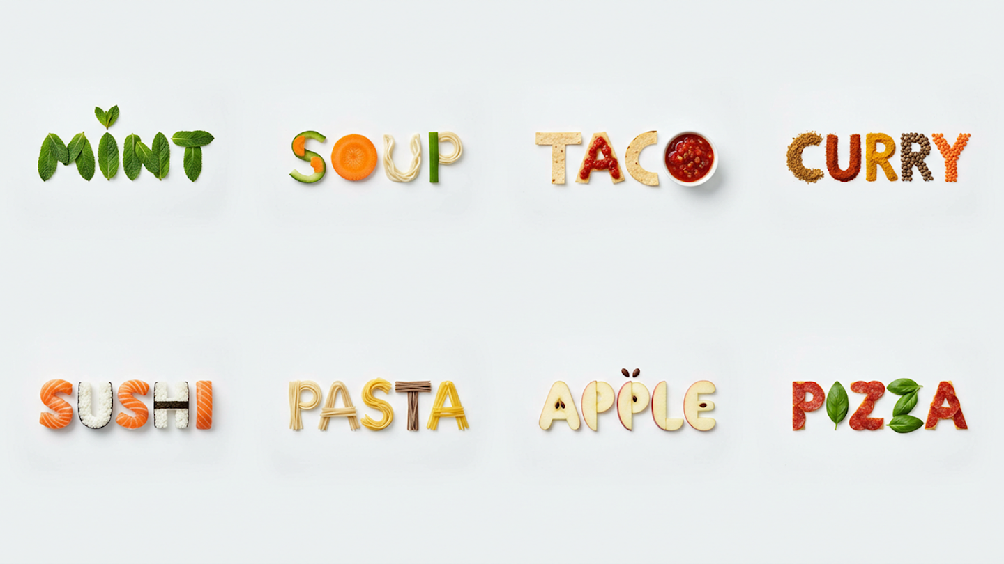 Eight words spelled out using the actual food items they represent: 'MINT' made of leaves, 'SOUP' using a bowl and noodles, 'TACO' made of chips, 'CURRY' made of spices, 'SUSHI' made of sushi rolls, 'PASTA' made of dry noodles, 'APPLE' made of fruit slices, and 'PIZZA' made of pizza ingredients.